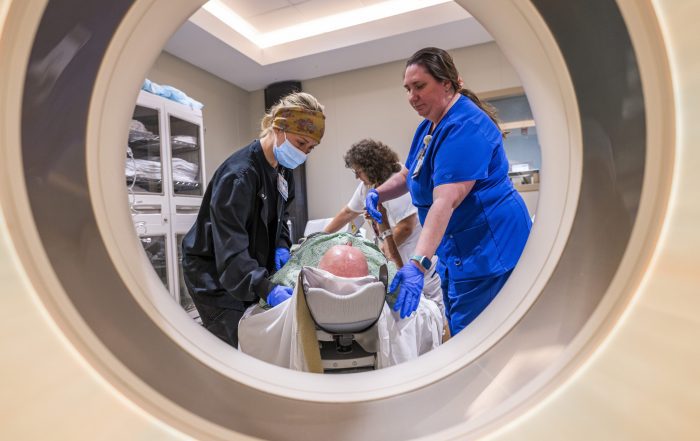 Three caregivers prepare a patient for a medical scan in a hospital.