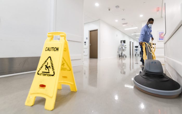 A caregiver operates an electric floor cleaner on a hospital floor.