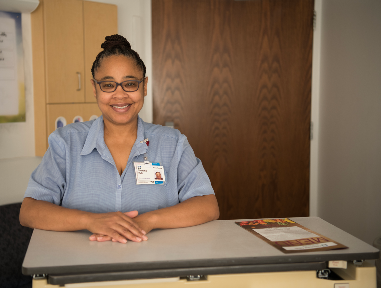 A woman Cleveland Clinic employee wearing a badge rests her elbows on a high desk-like surface in a hospital setting.