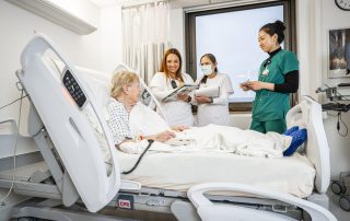 Three caregivers smiling as they work with a patient in a hospital room.