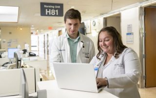 Two caregivers working together on a computer in a Med/Surg unit.