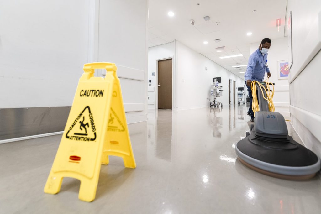 A caregiver operates an electric floor cleaner on a hospital floor.