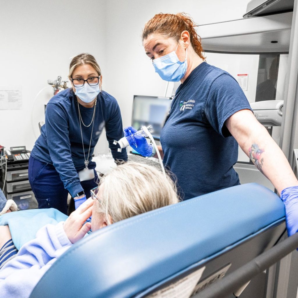 Two respiratory caregivers provide a breathing treatment to a patient in a hospital room.