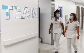Two Cleveland Clinic nurses in white scrubs and masks walk together down a hospital hallway past a wall display with the word TEAM.