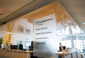 Reception area of Cleveland Clinic Canada with a large sign listing services including sports medicine, sports rehabilitation, specialist clinics, and express care.