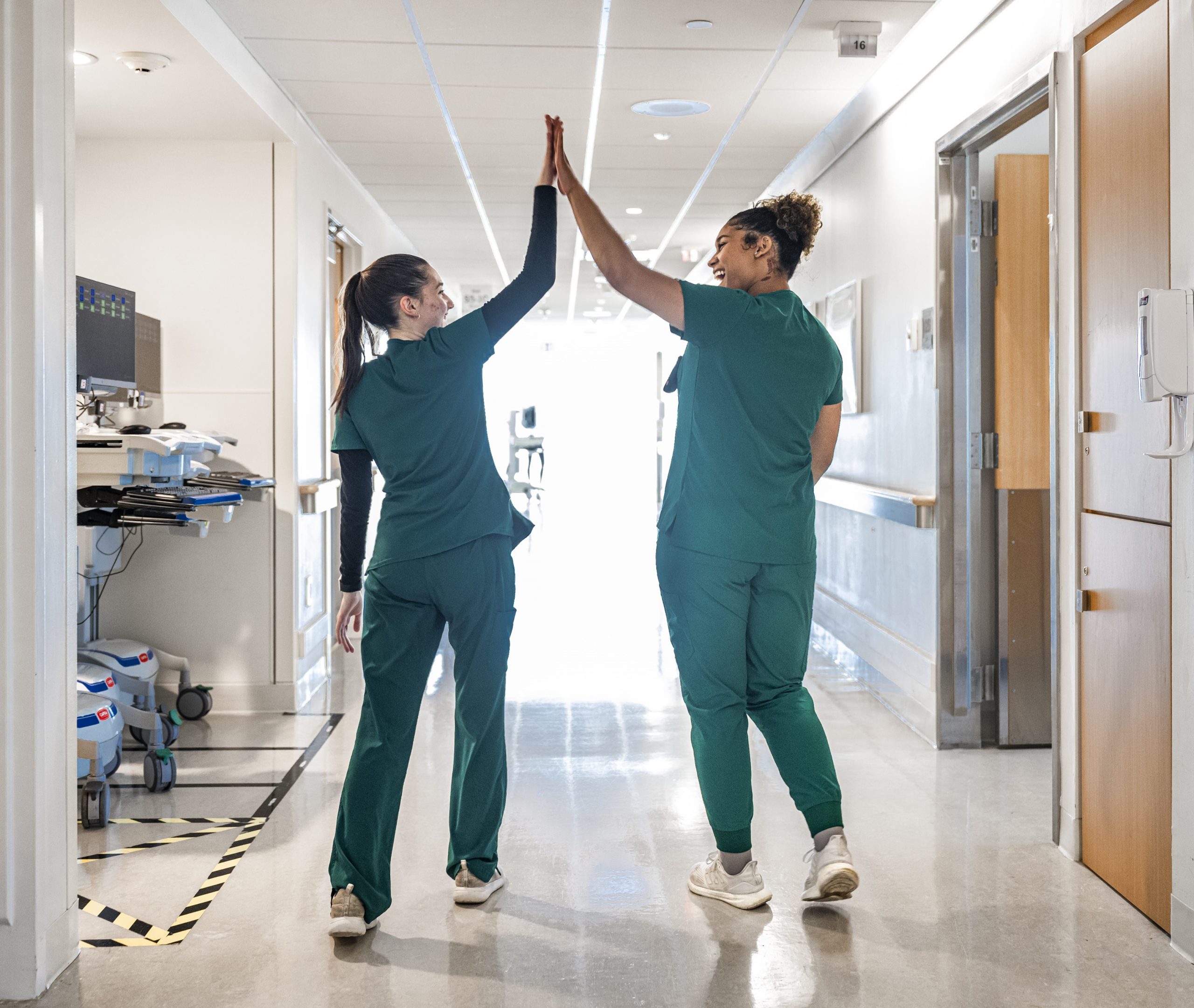 Two Cleveland Clinic nurses in green scrubs share a high-five while walking down a hospital hallway.