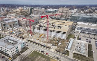 An aerial view of Cleveland Clinic’s campus shows a large construction site with cranes, adjacent to parking garages and hospital buildings.