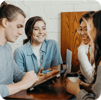 A group of four young adults sit together smiling and talking in a casual setting.